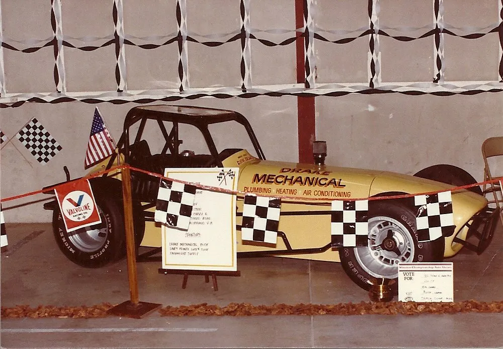 A yellow Drake Mechanical race car on display at a 1982 car show