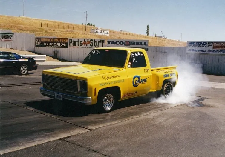 A yellow Drake-sponsored pickup doing a burnout at a drag strip