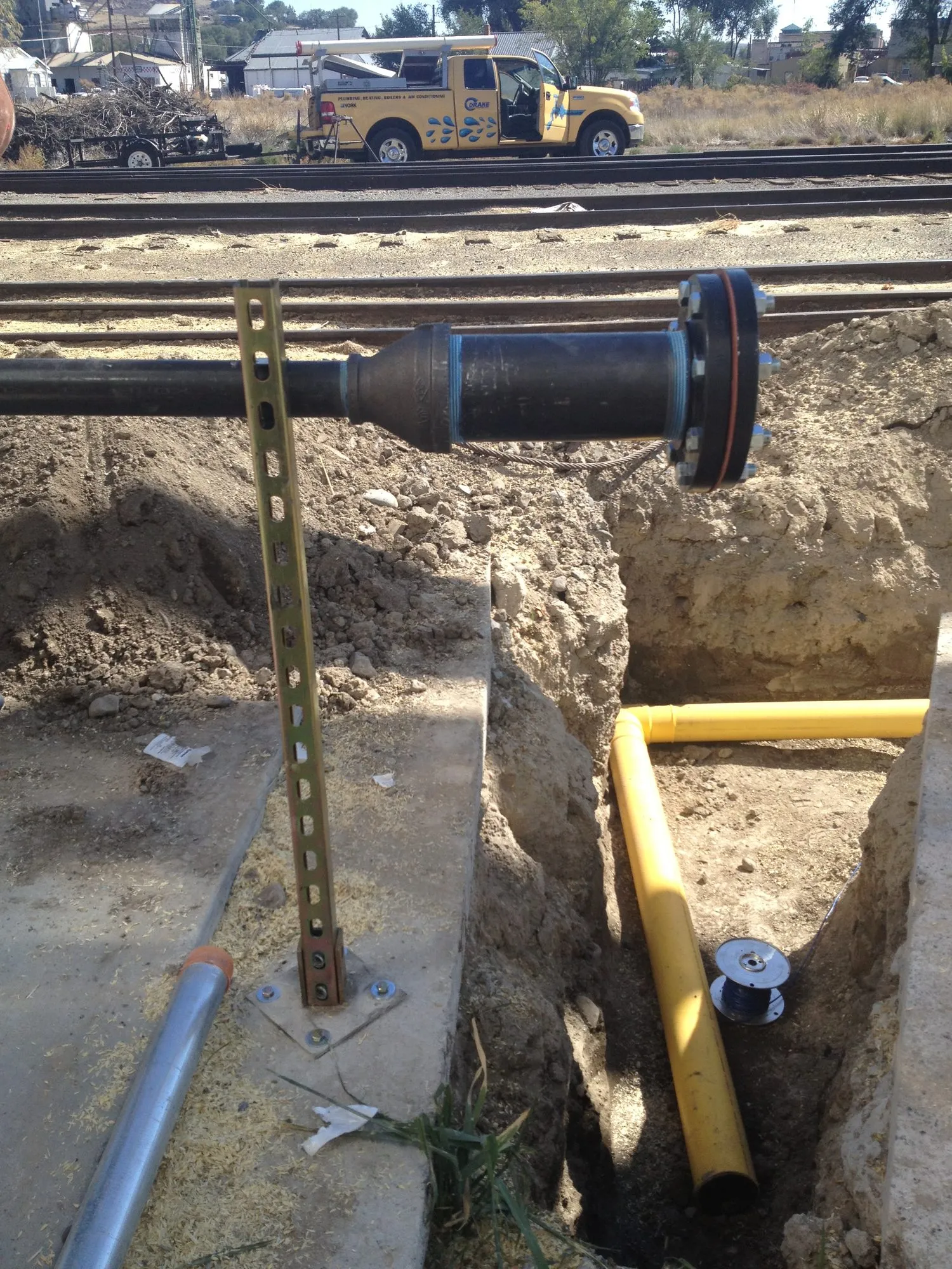 A yellow gas line in a trench, with a Drake Mechanical truck in the background